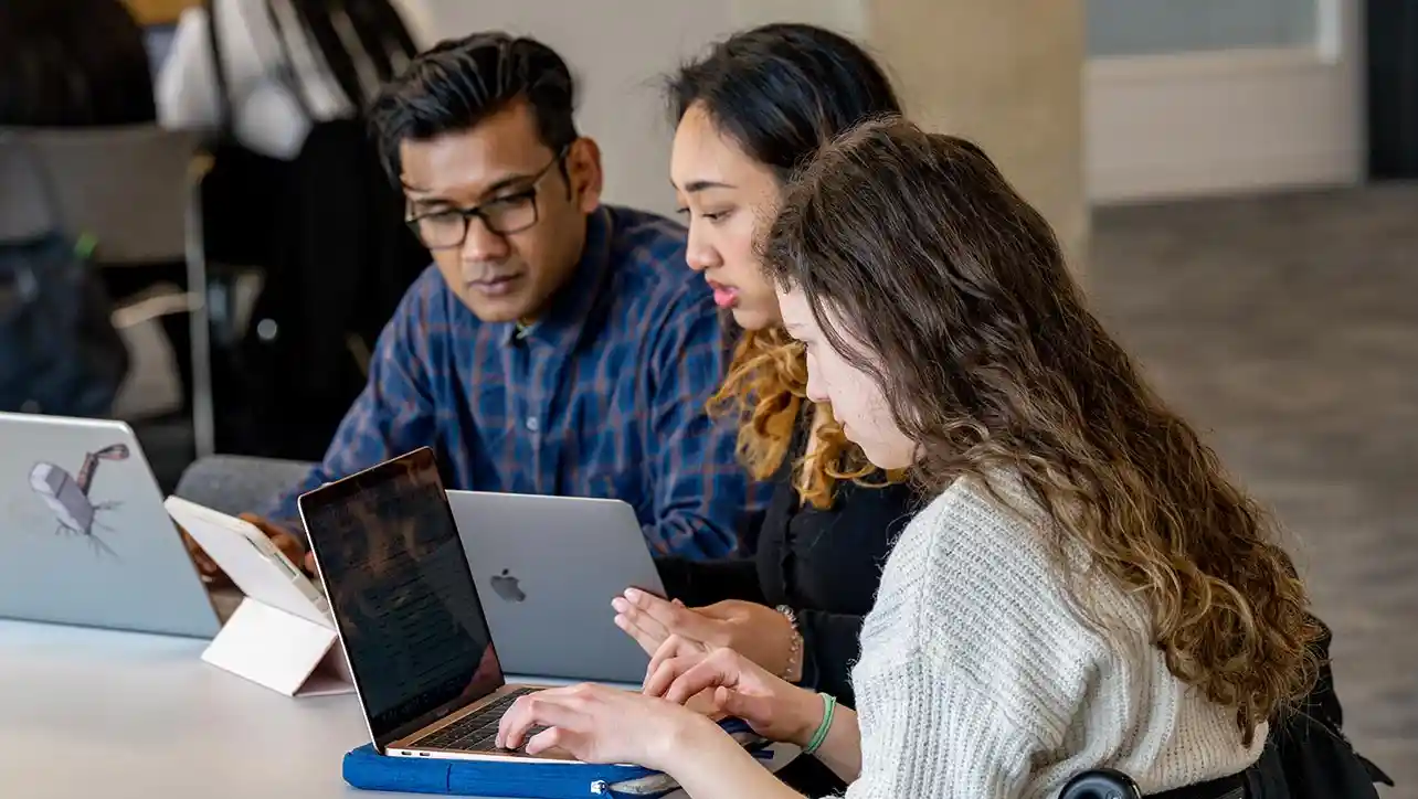 Group of students sat at a table with laptops.