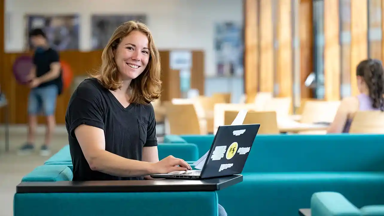 A University of Southampton student smiling to camera, sat down and working on a laptop.